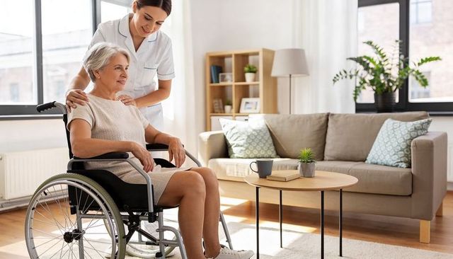 Female caregiver assisting senior woman in wheelchair at home, compassionate daily home care