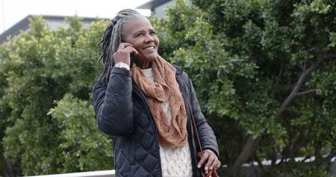 Senior african american woman talking on phone on urban balcony wearing scarf and jacket