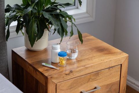 Minimalist wooden bedside table with houseplant, pill bottles, thermometer and water glass
