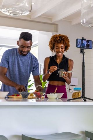 African american couple making healthy breakfast bowls in modern kitchen, filming content