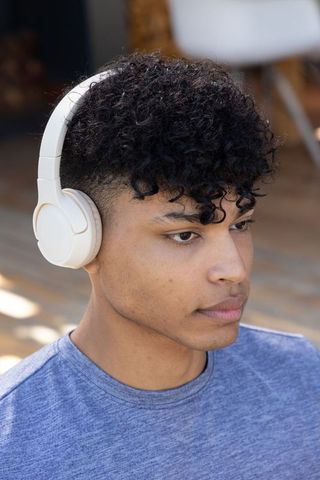 Young african american man listening with white wireless headphones on sunlit deck