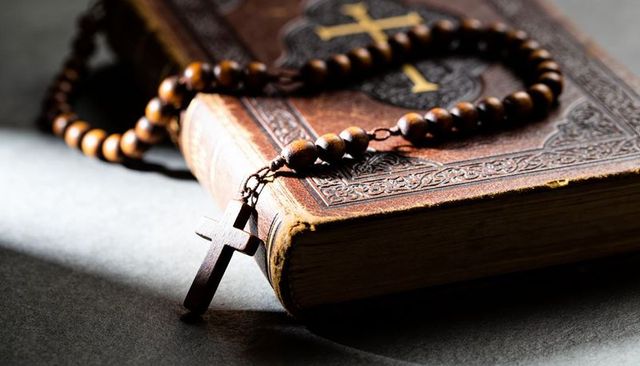 Vintage leather bible with wooden rosary and cross on dark tabletop