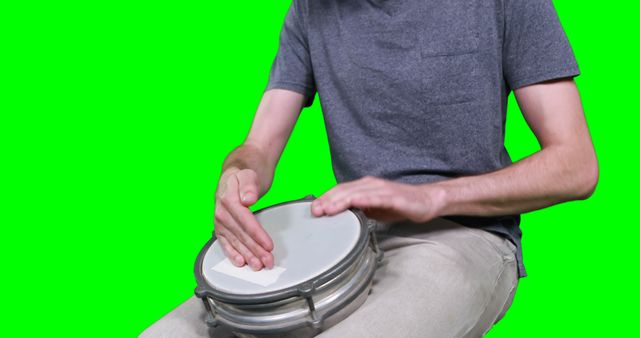 Mid section of drummer playing drum against green screen