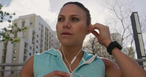 Adjusting earbud while preparing for urban run wearing turquoise top and smartwatch