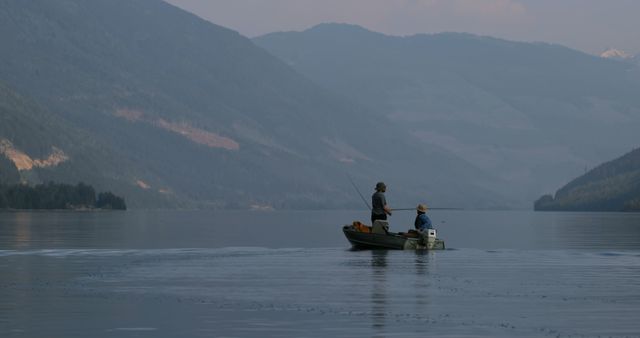 A couple enjoys fishing from a boat on a calm lake surrounded by mountains. This image is perfect for travel brochures, outdoor adventure advertisements, and relaxation-themed blog posts.