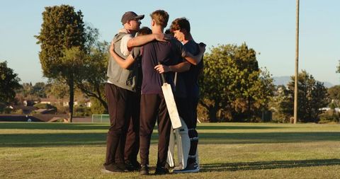 Diverse cricket team huddling with coach for pep talk during golden hour practice