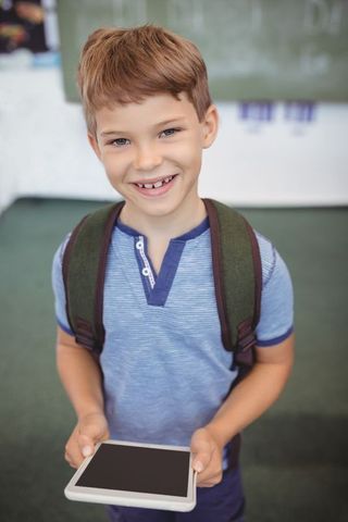 Smiling Schoolboy Holding Tablet in Classroom Environment