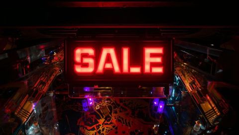 Glowing red sale sign lighting pinball playfield with vibrant leds and reflective ramps