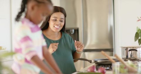 African american mother watching child chopping vegetables in bright family kitchen