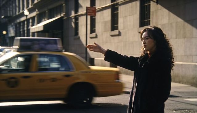 Woman hailing taxi on sunlit urban street wearing dark coat city commuter moment