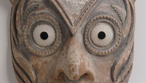 Antique carved wooden mask with woven eye inlays showing patina and textured pigments