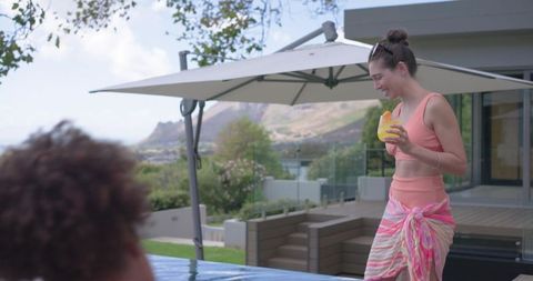 Diverse female friends enjoying poolside cocktails, sarong style and mountain view on sunny patio