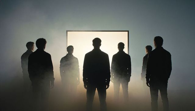Seven silhouettes facing glowing portal in misty studio with dramatic backlight