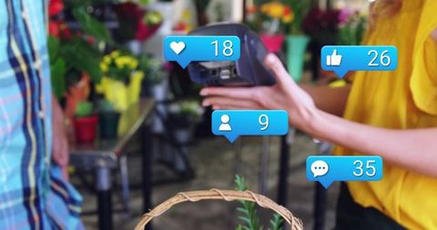 Florist holding card reader at market while social media engagement icons float overhead