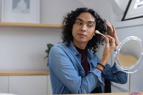 Non-binary person applying makeup at vanity mirror practicing daily self-care ritual