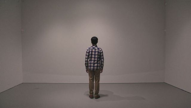 Solitary man standing facing blank gallery wall under spotlight minimalist interior scene