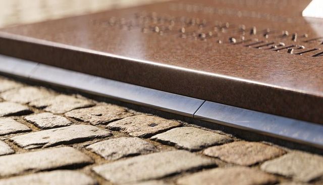 Engraved granite memorial edge meeting historic cobblestone pavement with metal trim