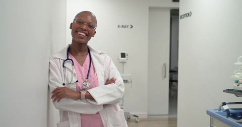 Smiling african american clinician leaning in corridor wearing lab coat and stethoscope
