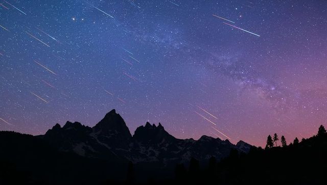 Shooting stars and milky way streaming over jagged mountain silhouette at twilight