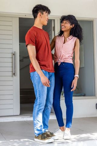 Smiling young couple greeting at modern home entrance, casual porch welcome