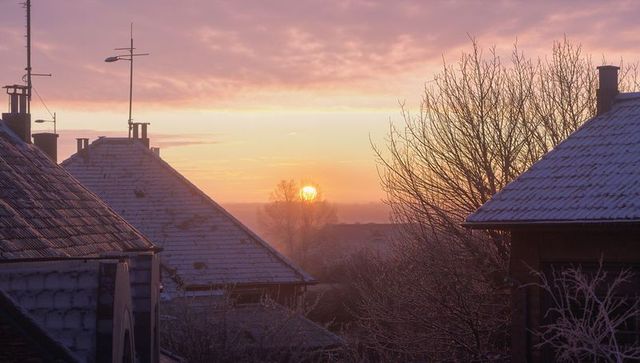 Winter sunrise over suburban rooftops bathing frosted tiles in pastel dawn light