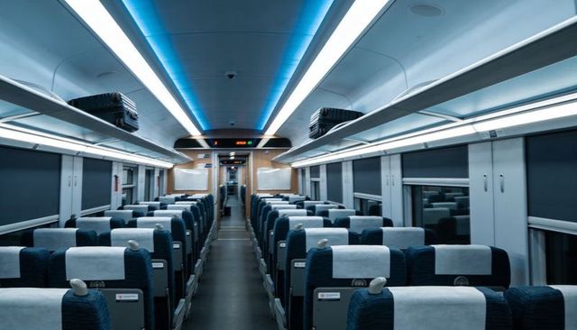 Modern high-speed train interior featuring paired reclining seats, blue led aisle lighting
