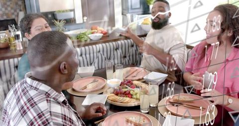 Friends enjoying casual brunch around kitchen table sharing cheese board and refreshing drinks