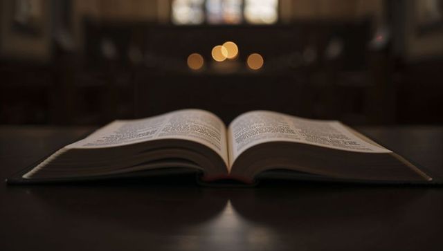 Open bible resting on wooden lectern with warm candle bokeh in chapel interior