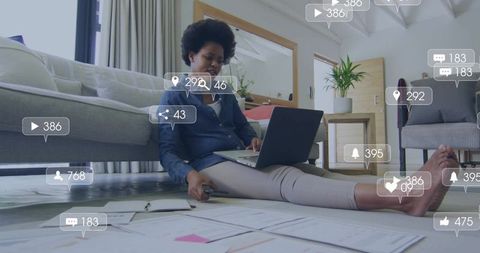 Working woman sorting documents on living room floor with laptop and social media icons