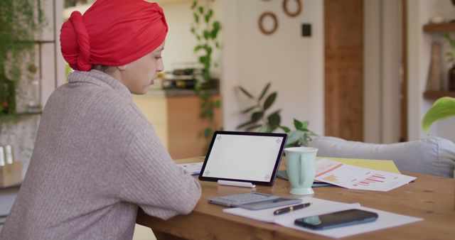 Image of biracial woman in hijab sitting at desk at home, working on laptop, copy space on screen. Remote working, communication, inclusivity and domestic life.
