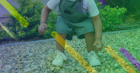 Toddler squatting on gravel picking pebbles in garden overalls white sneakers