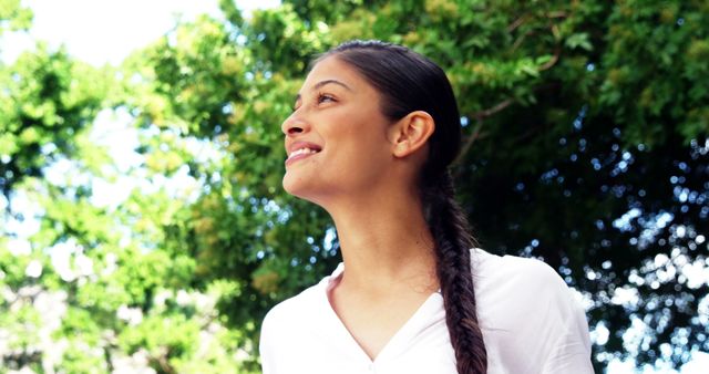 A young woman of Hispanic ethnicity looks up optimistically, with copy space. Her bright expression and the outdoor setting suggest a sense of hope or anticipation.