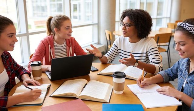College students collaborating around campus study table with laptop, books and coffee