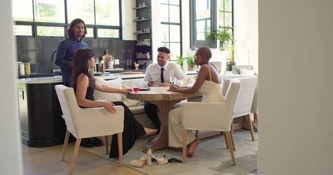 Friends Gathering Around Kitchen Table Enjoying Drinks, Laughter, and Casual Conversation