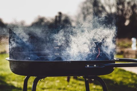 Backyard charcoal grill producing thick smoke over hot coals on sunny green lawn
