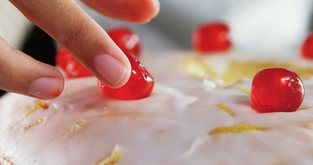 Close-up of woman topping a fresh baked cake with cherry 