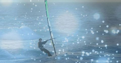 Windsurfer carving waves under green sail, leaning back on open ocean with sea spray