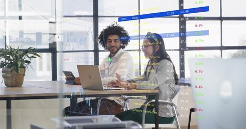 Colleagues collaborating on laptop analyzing market charts overlay in modern office
