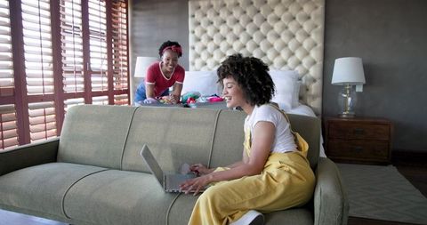 Woman in Yellow Overalls Enjoying Remote Work in Cozy Living Room