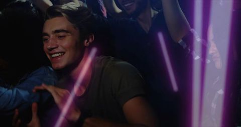 Smiling young man reaching through neon nightclub crowd with led beams