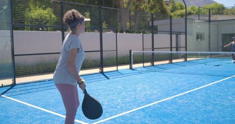 Woman playing padel on bright blue court wearing visor and pink leggings outdoor sport