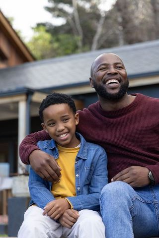 African american father and son sitting on porch steps smiling, sharing joyful family moment