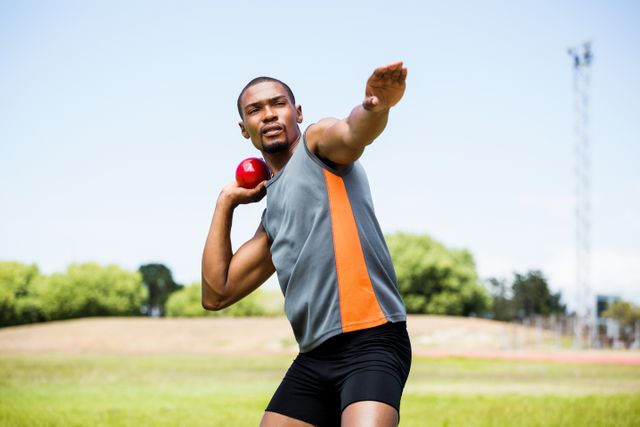 Male athlete preparing to throw shot put ball in outdoor stadium. Ideal for use in sports-related content, fitness promotions, athletic training programs, and motivational materials. Highlights strength, focus, and determination in competitive sports.