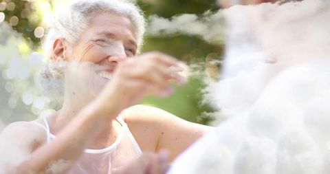 Smiling senior woman reaching for partner in sunlit garden, joyful couple sharing moment