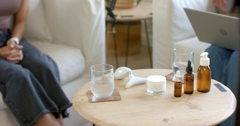 African american women comparing skincare on wooden table with laptop and massager