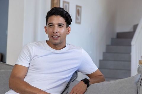 Young african american man relaxing on modern sofa in minimalist neutral home interior