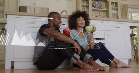 Couple relaxing on kitchen floor drinking coffee with data analytics overlay
