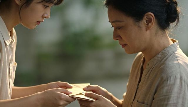 Two women exchanging envelopes, leaning close in tender courtyard moment, closeup faces