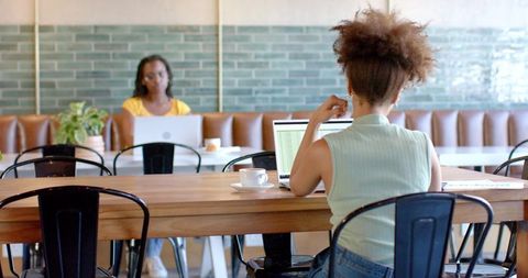 Remote professional typing on laptop in bright cafe coworking space with coffee and focus