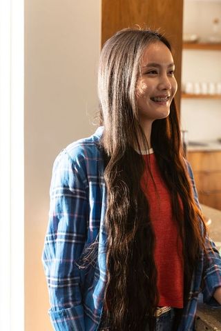 Asian woman with long hair enjoying sunlit kitchen moment